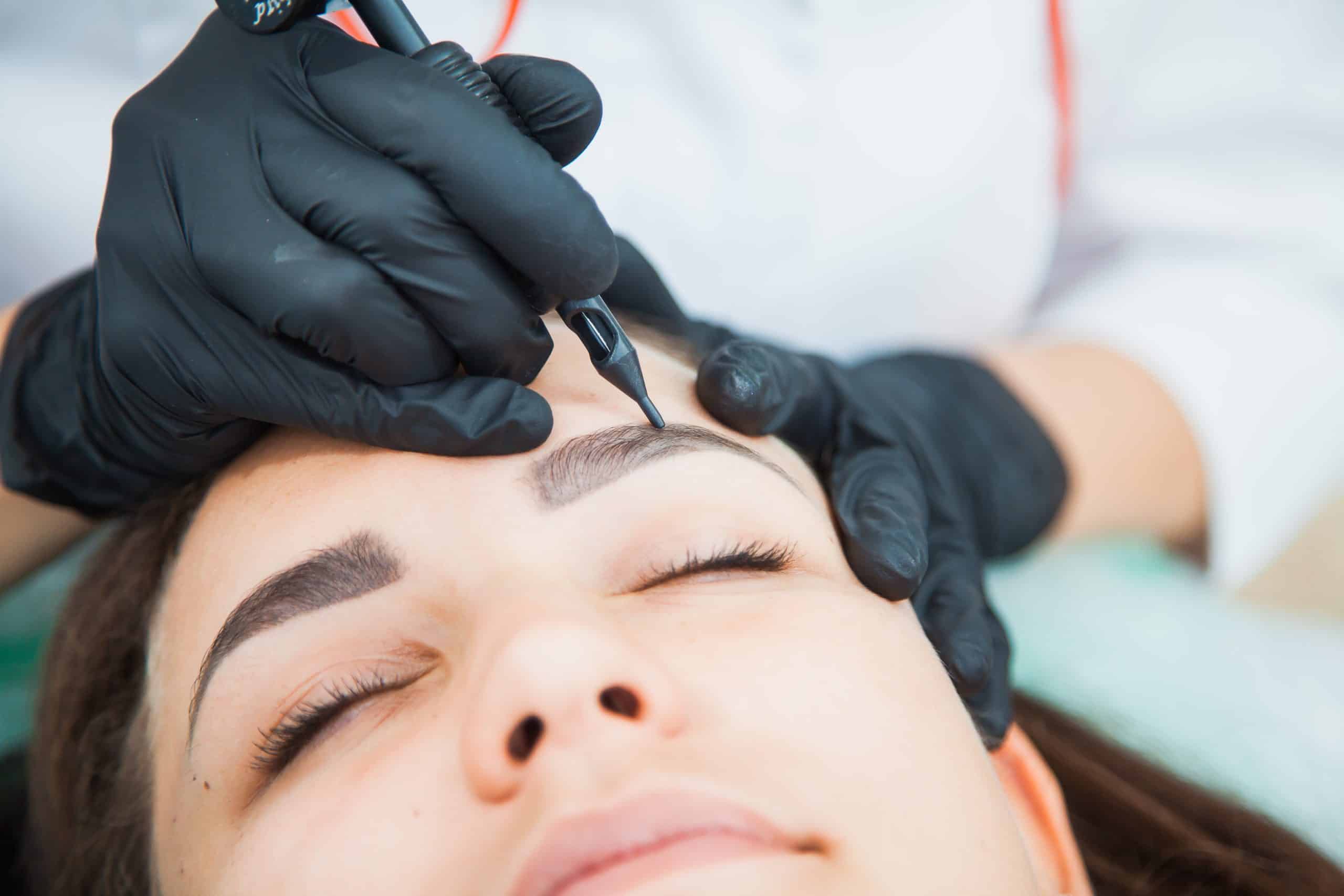 Young woman on permanent make-up procedure, tattooing eyebrows in natural tint. Eyebrow Correction closeup. Beauty Concept.