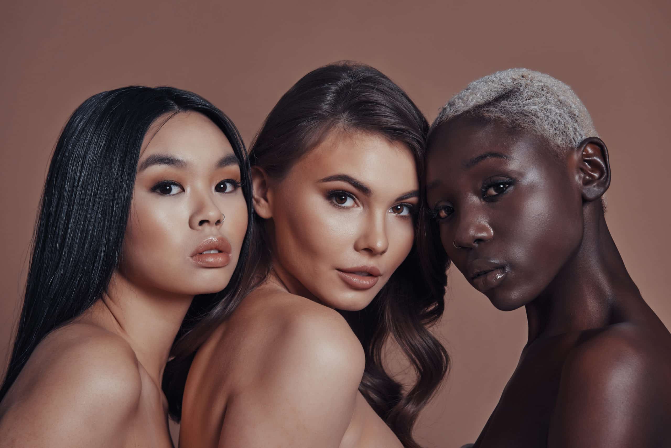 Our Culture Unforgettable beauty. Three attractive young women looking at camera while standing against brown background
