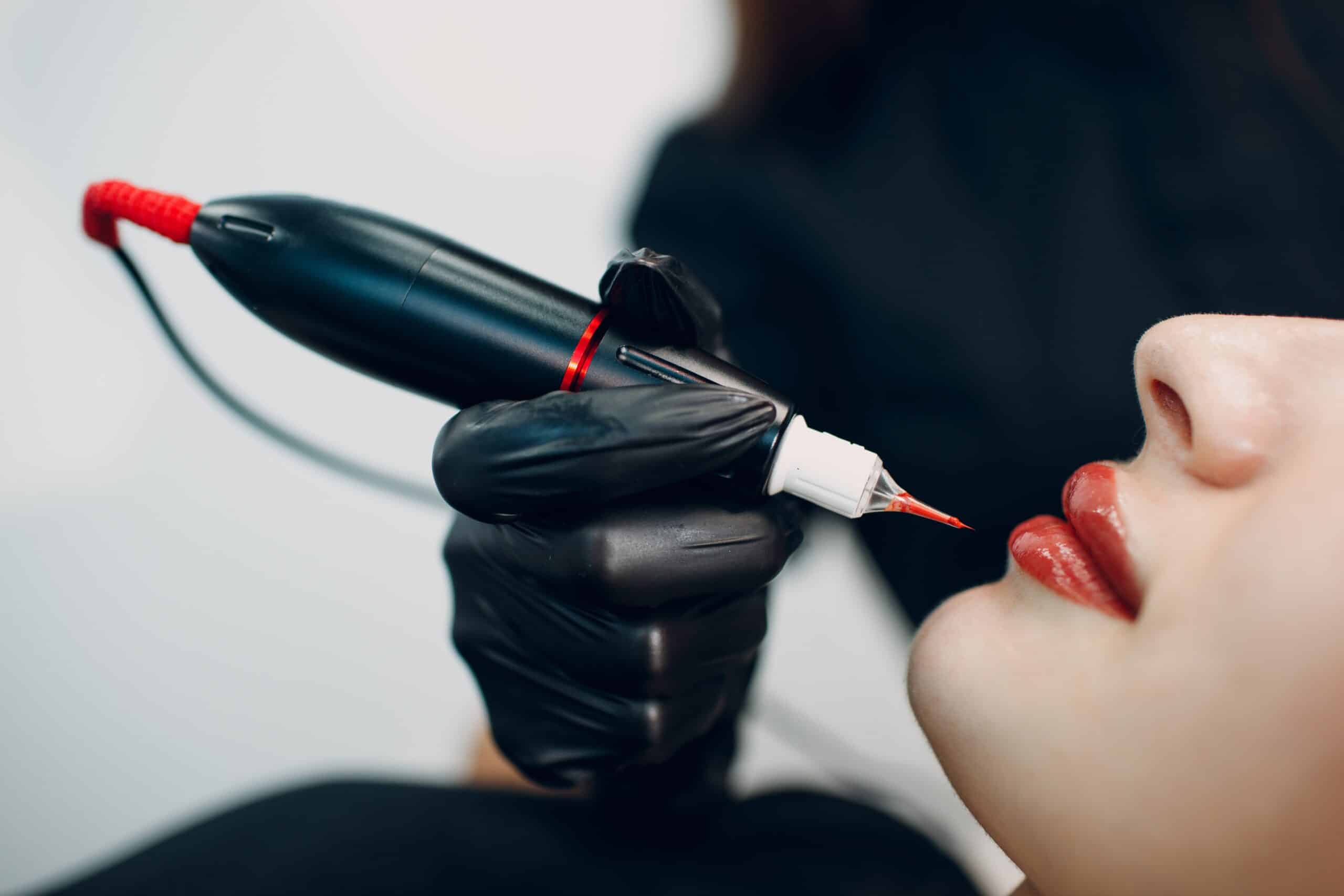 Cosmetologist applying red permanent make up tattoo on female lips.