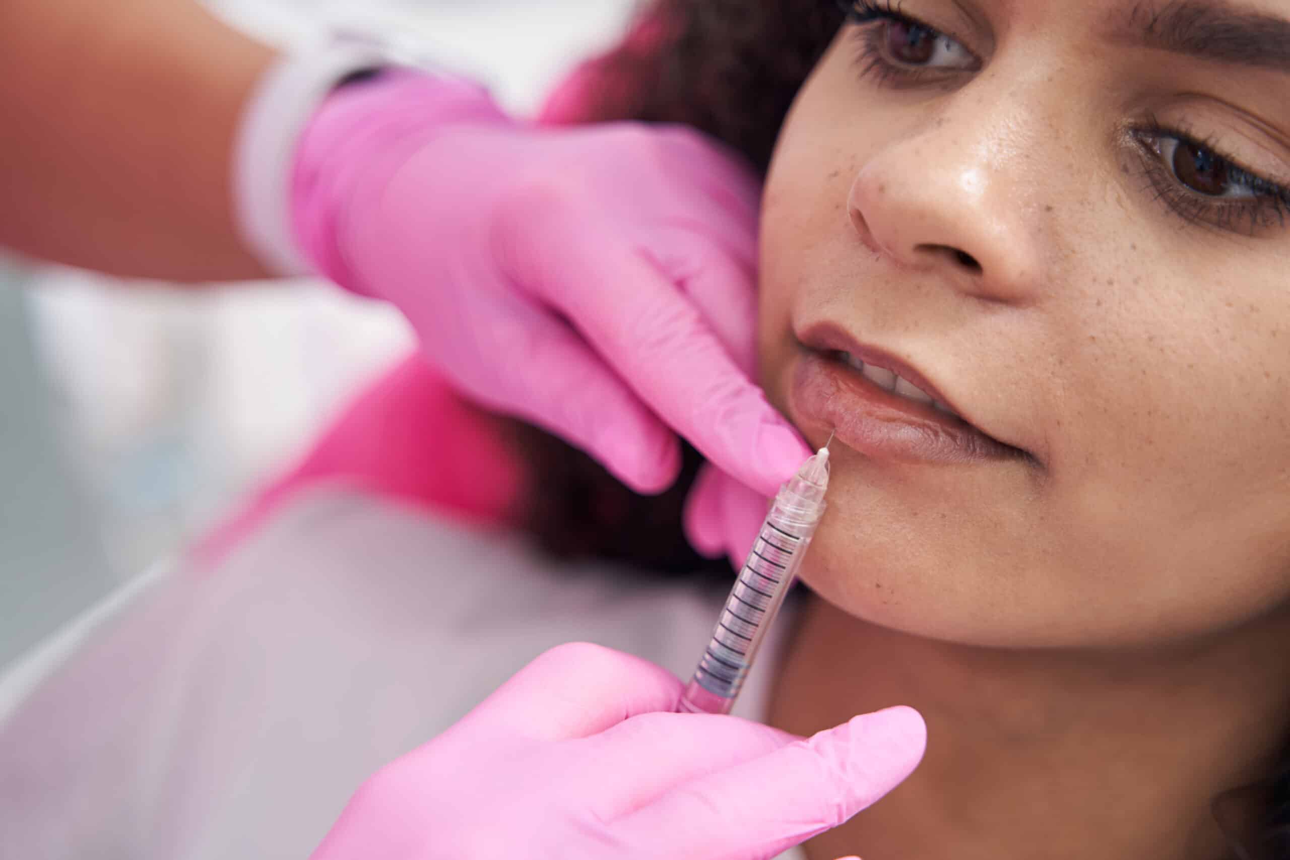 Focused lady lies on beauty procedure while doctor injects her lip plumper